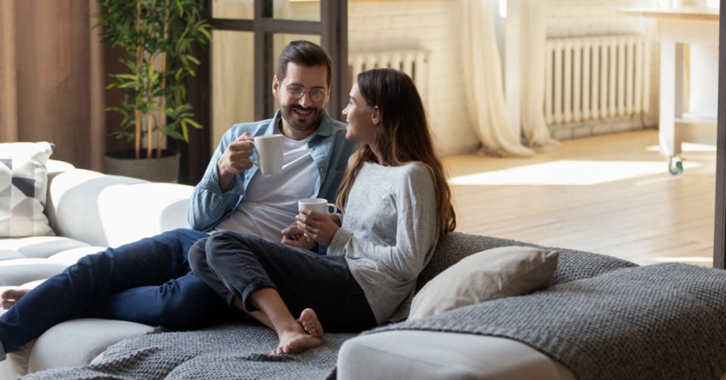 a couple sitting on couch drinking coffee looking at each other happily